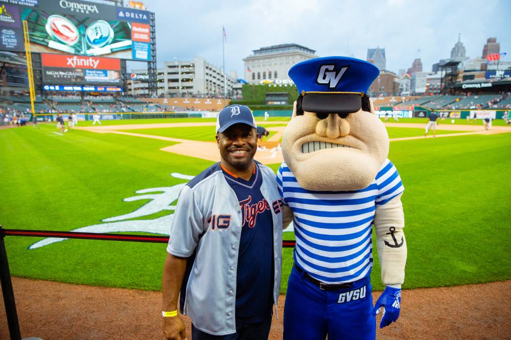 A gsvu alumni in tigers gear is posing with louie on the infield